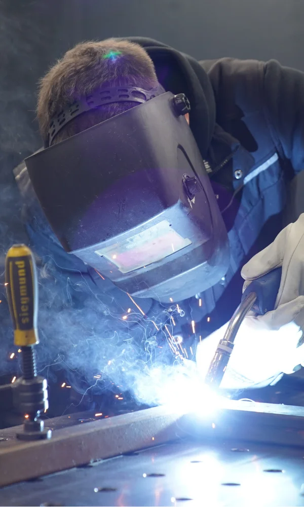 Schweißer mit Schutzhelm und Handschuhen beim Lichtbogenschweißen von Metall mit Funkenflug