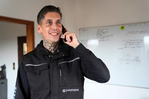 Daniel Wenz in Arbeitsjacke lächelt und telefoniert vor Whiteboard im Büro