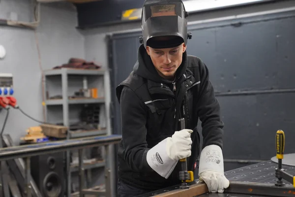 Schweißer in Metallwerkstatt mit Schutzhelm und Handschuhen beim Fixieren und Schweißen von Stahlbauteilen