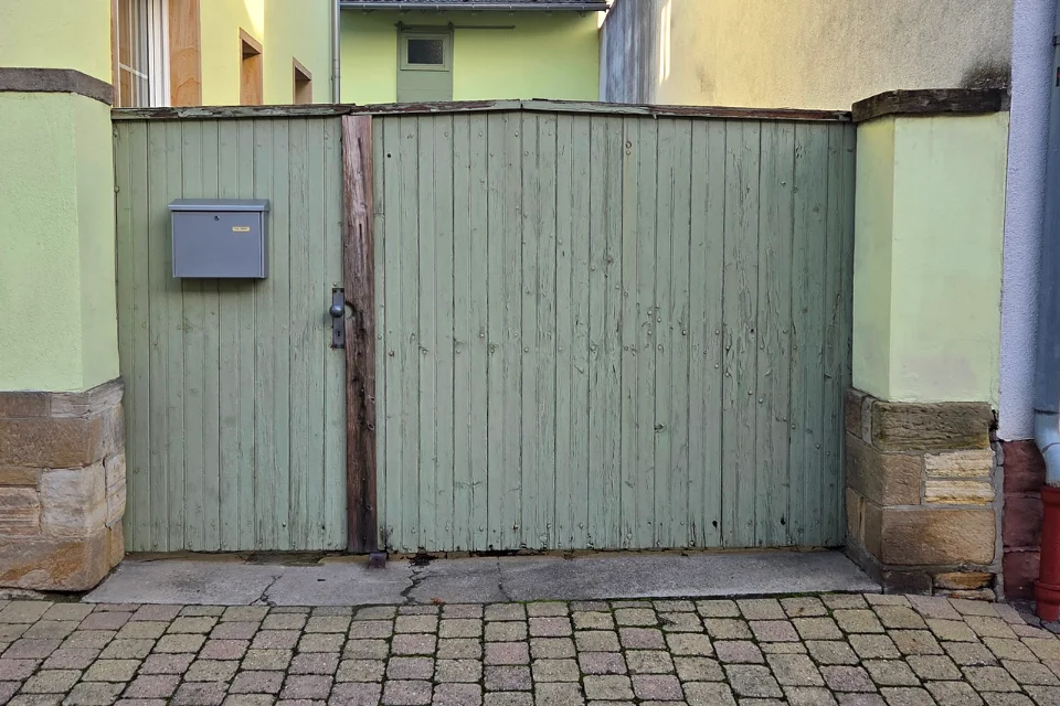 Grünes altes Holztor mit Briefkasten zwischen Sandsteinpfeilern vor Kopfsteinpflaster