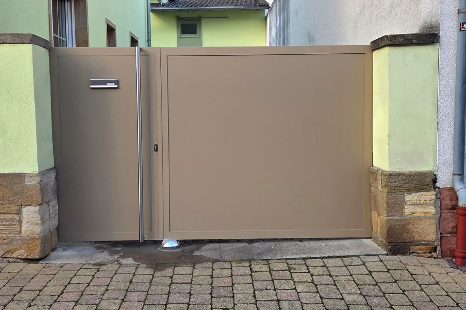 Metall-Einfahrtstor in Beige mit Nebentür, Briefkasten, Sandsteinpfeilern und gepflasterter Einfahrt
